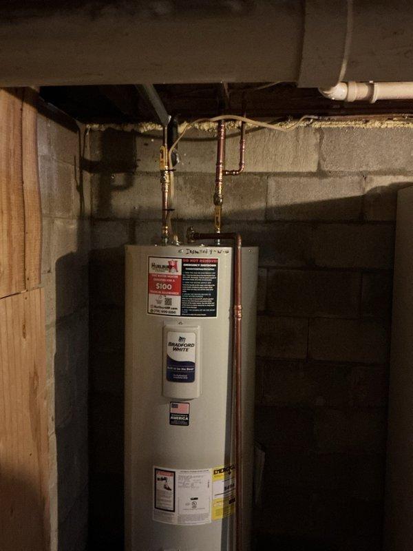Responded to emergency water heater failure caused by tank leak that allowed water to contact electrical connections, creating a sparking hazard. Upon inspection, confirmed the existing water heater had failed due to bottom tank corrosion and active leaking, making repair unsafe and unfeasible. Removed and properly disposed of the failed unit. Installed new Bradford White residential tanked water heater in basement location against concrete block wall. Connected copper supply lines to top of unit with brass fittings and shut-off valves. Verified all plumbing connections for proper seal and tested system operation. Installation completed per manufacturer specifications and local plumbing codes.