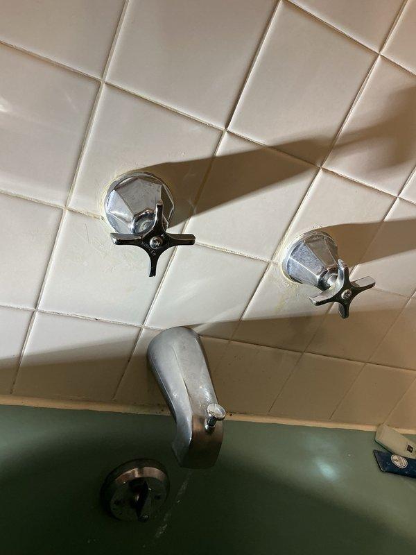 Responded to bathtub faucet leak in owner-occupied residence. Upon inspection, identified dripping from both the tub spout and cold water handle of vintage three-handle faucet assembly mounted on tiled wall above green bathtub. Measured existing fixture spacing and documented worn components showing signs of age and deterioration. Completed part order form to procure replacement parts for repair of leaking faucet components.