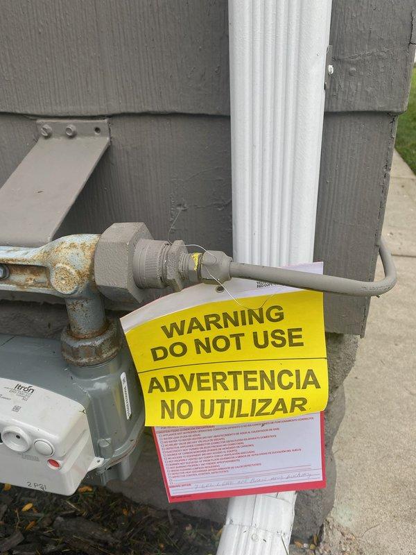 Responded to gas leak emergency previously identified and tagged by utility company on exterior gas main line. Documented hazardous condition with warning tags visible on weathered, corroded gas piping at meter location. No interior gas odor detected during inspection, confirming leak isolated to exterior system. Coordinated scheduling with licensed plumber for repair work to address utility-marked leak location.