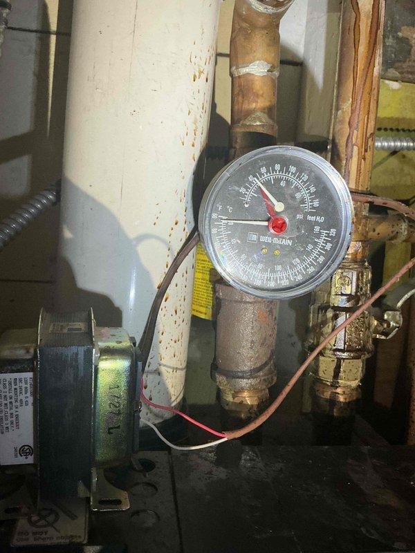 Responded to no-heat call on 3-year-old boiler system with radiator heat distribution. Upon inspection, found control board sustained water damage from overhead leak, resulting in complete loss of power to unit and non-functional display screen. This marked the second occurrence of water-related damage to the electrical components. Documented system condition showing internal mechanical compartment with expansion tank, circulator pump, copper piping, and compromised control board requiring replacement to restore heating operation.