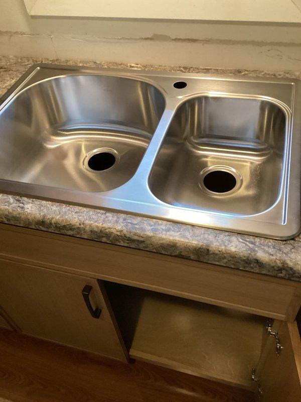 Installed stainless steel double-basin kitchen sink with single-handle faucet mounting preparation in laminate countertop. Customer provided sink and faucet components; fresh PVC drain pipes were supplied per customer request to replace existing plumbing connections. Final faucet installation was postponed pending customer's decision on service pricing.
