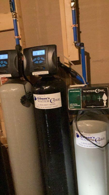 Completed comprehensive plumbing inspection of residential property. Evaluated bathroom plumbing installation including wall-mounted water supply connections with braided metal supply lines and access panel in hexagonal tile surround. Inspected whole-house water treatment system consisting of dual-tank water softening and filtration equipment with digital control units, verified proper operation of system components, and confirmed all plumbing connections and PVC piping were secure and functioning correctly.