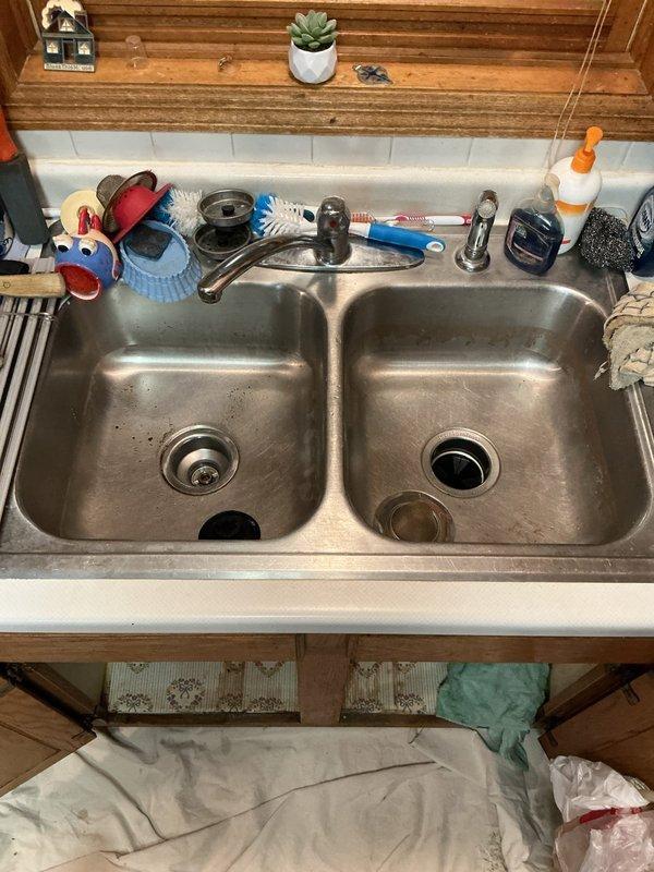 Responded to a clogged kitchen sink drain with standing water that would not drain. Upon diagnostic inspection, discovered a blockage located deep within the drain line that required mechanical cabling, and identified a leaking basket strainer on the left basin. Cabled the entire kitchen drain line to clear the obstruction and restore proper flow. Removed and replaced the defective basket strainer on the left side of the double-basin sink. Replaced all tubular drain piping under the sink to ensure leak-free operation. Tested both basins for proper drainage and verified no leaks were present at any connections. All fixtures functioning properly upon completion.