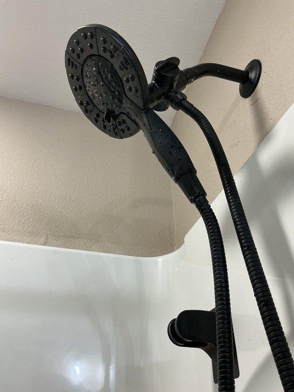 Responded to water leak spraying from shower arm pipe extending from wall. Upon inspection, discovered damaged and smashed threads on existing shower arm preventing proper seal. Removed defective shower arm and found threads severely compromised, requiring partial thread removal to achieve clean connection surface. Installed replacement shower arm and restored proper water flow to dual-head black shower system without leakage.