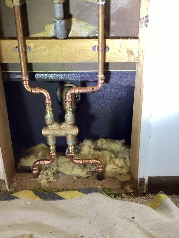 Completed comprehensive hose bib replacement and plumbing upgrades including installation of frost-free 3/4" hose bib on front of house and replacement of threaded 3/4" hose bib on rear of house. Added stop and drain valves on piping in ceiling for improved water control and winterization capabilities. Installed Precision Plumbing Products pressure balancing valve (ASSE 1016 compliant) on two-handle tub/shower valve system accessed through wall cavity behind shower fixture. During service, discovered main water valve was inoperative and required alternative water control methods to complete installations. All copper supply lines were properly connected using push-fit brass fittings to new valve assemblies. Work performed in basement ceiling area with notation that installed components will require relocation when basement ceiling finishing occurs in future. Submitted parts requisition form for required materials and documented main valve failure for future repair scheduling.