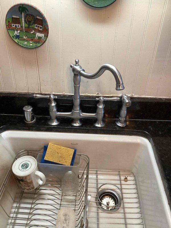 Responded to kitchen faucet sprayer malfunction where the decorative escutcheon and mounting components had separated from the base unit, leaving no adequate surface for secure attachment. Upon inspection, determined that the sprayer assembly lacked proper structural support for permanent repair. Disconnected the compromised faucet components and provided temporary support to the sprayer parts. Documented the existing bridge-style faucet configuration with chrome finish and completed parts sourcing form to facilitate replacement of the damaged sprayer assembly and mounting hardware.