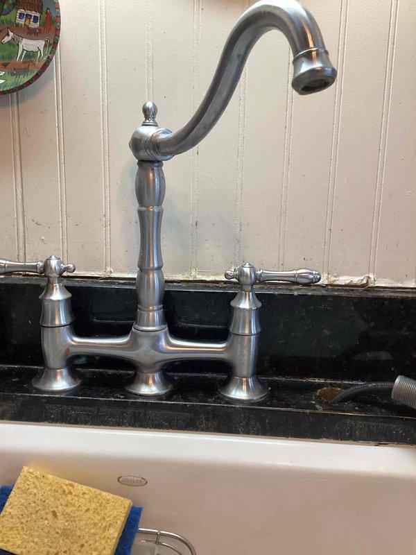 Responded to kitchen faucet sprayer malfunction where the decorative escutcheon and mounting components had separated from the base unit, leaving no adequate surface for secure attachment. Upon inspection, determined that the sprayer assembly lacked proper structural support for permanent repair. Disconnected the compromised faucet components and provided temporary support to the sprayer parts. Documented the existing bridge-style faucet configuration with chrome finish and completed parts sourcing form to facilitate replacement of the damaged sprayer assembly and mounting hardware.