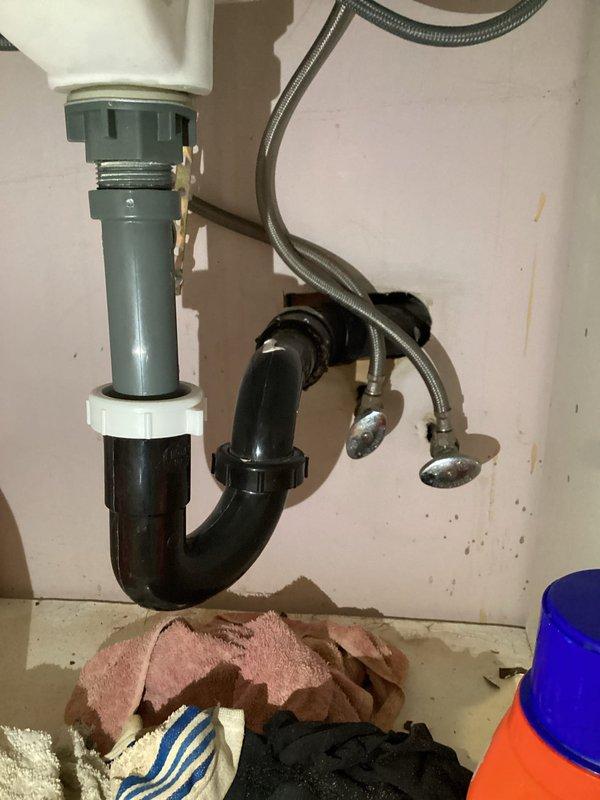 Completed comprehensive plumbing inspection to verify quality of recent repair work. Inspection revealed multiple issues requiring attention, including faucets and garbage disposal that need replacement. Documented under-sink plumbing configuration showing standard P-trap drainage assembly with braided flexible water supply lines, and basement floor drain installation with PVC piping connections in progress.