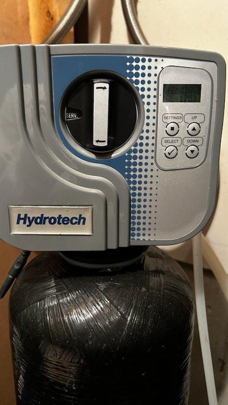 Responded to service alert on Hydrotech water softener system for new homeowner. Inspected water softener unit and reverse osmosis system for operational status and potential service issues. Found "FROZEN FILTER" alert displayed on control panel but determined no immediate mechanical failures present. Documented system condition with photos showing properly mounted equipment and functional control display. Coordinated with service advisor for follow-up water quality testing and comprehensive equipment verification to ensure optimal system performance.