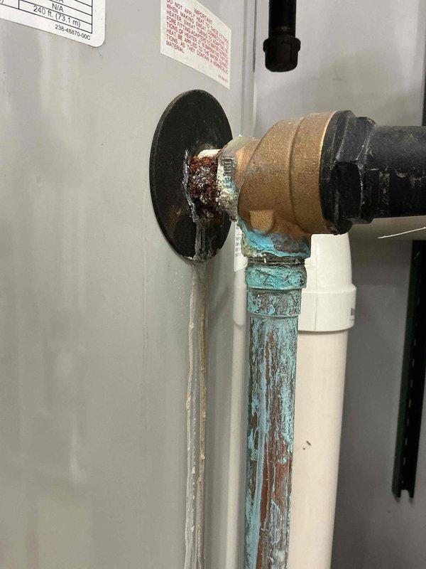 Responded to commercial water heater leak complaint and performed inspection of two water heaters. Upon arrival, identified active drip leaks at copper intake water pipes on both units, with visible corrosion, mineral deposits, and turquoise-blue oxidation patterns indicating ongoing water seepage. Documented conditions with photographs showing corroded brass fittings, deteriorated pipe connections, and water damage staining on equipment panels. Coordinated with maintenance management and submitted findings for repair estimate preparation.