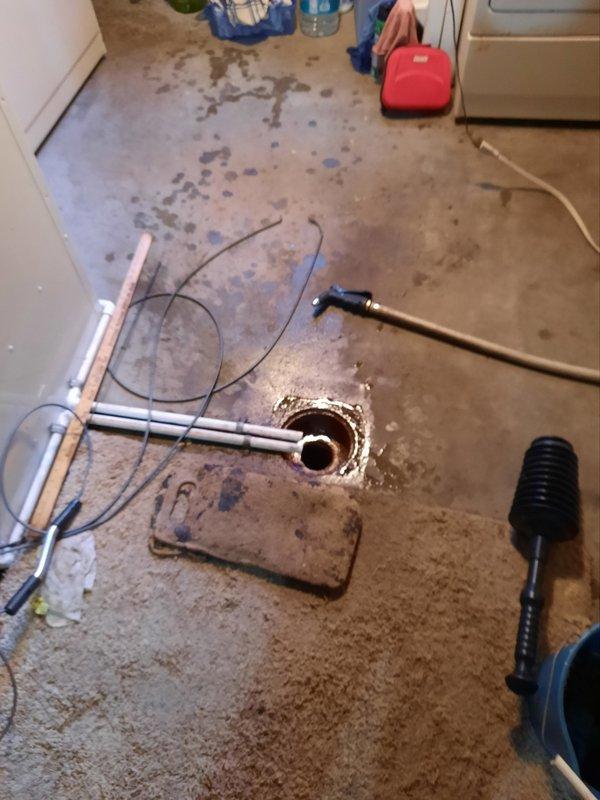 Responded to basement floor drain backup with water accumulation in laundry area. Located soft plug obstruction approximately 10 feet from access point in drainage line. Successfully cleared blockage using mechanical snake equipment, restoring proper drainage flow. Obstruction was positioned beyond 90-degree pipe bend, requiring specialized technique to navigate turn and reach clog. Water damage visible on laundry room floor from backup prior to service. Drain tested and confirmed flowing freely after clearance completed.