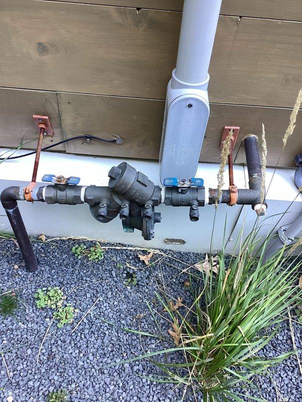 Completed biannual preventive maintenance inspection including exterior faucet drainage and testing, comprehensive leak detection throughout the property, water heater maintenance and cleaning, sump pump inspection, and laundry hose evaluation. Inspected outdoor plumbing assembly featuring backflow preventer, ball valve, and associated copper fittings mounted along exterior foundation. Examined AO Smith water heater installation including expansion tank, pressure relief valve, and all supply and discharge piping connections. One issue identified during inspection requiring repair; provided estimate for corrective work to be scheduled separately.
