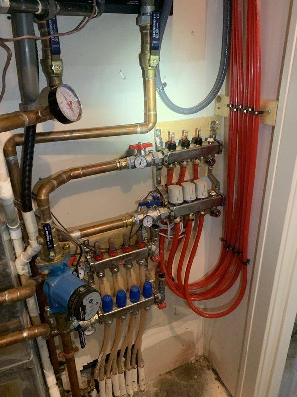 Replaced corroded 3-loop hydronic manifold serving upstairs bathroom zones and leaking pump flange on one heating zone. Cleaned corrosion from affected piping, reconnected all distribution lines to new manifold assembly, and purged air from the system. Set system pressure to 18 psi, replaced thermostat batteries, and cycled all zones to verify proper operation with no leaks detected.