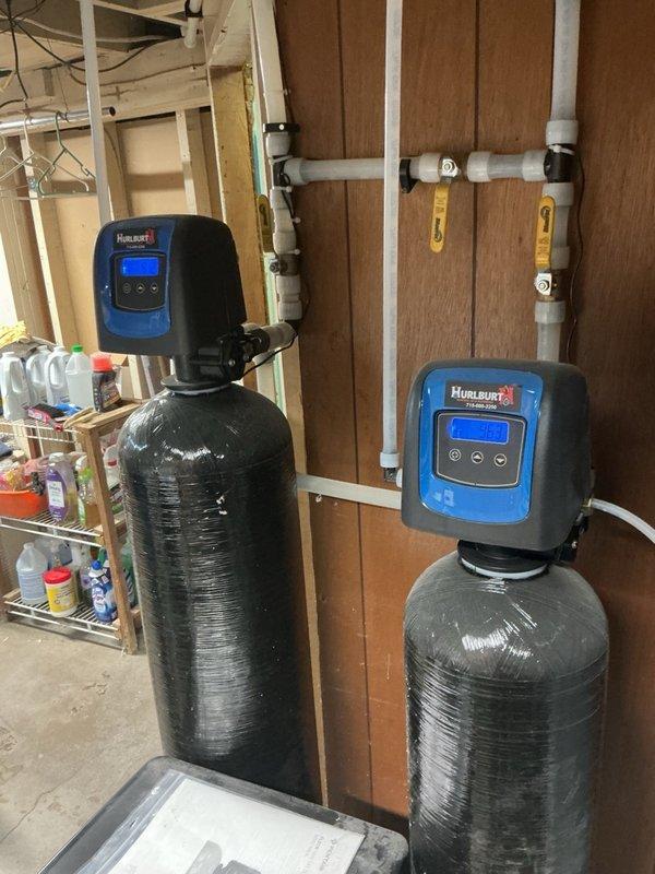 Completed annual family rewards plumbing inspection of water heater and water softener system. Inspected dual Hague water softener tanks with digital control heads, verified proper operation of control valves and shut-off points, and checked salt levels in softener units. Examined PVC drainage system installation including main vertical drain pipe with rubber coupling connectors and associated branch lines. All plumbing components found to be functioning properly with no immediate service needs identified.