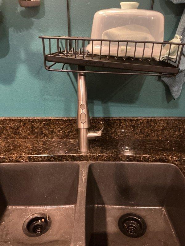 Responded to a leaking kitchen faucet in the mother-in-law suite where both the main faucet and sprayer were leaking during operation. Upon inspection, determined the existing kitchen faucet had reached end of life and was beyond economical repair. Removed the old faucet assembly and installed a new modern pull-down kitchen faucet with single-handle control mechanism between the double basin composite sink, restoring full functionality to the kitchen plumbing system.