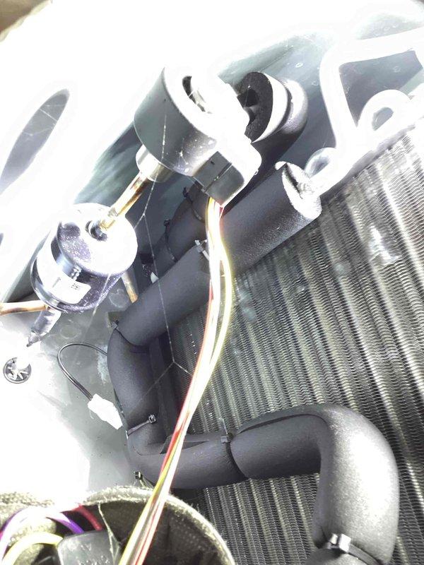 Replaced faulty thermistor on evaporator discharge coil with correct part. The grey-wired thermistor was removed from the evaporator coil assembly near the blower motor, and the new component was properly installed and secured to restore accurate temperature sensing functionality for the HVAC system.