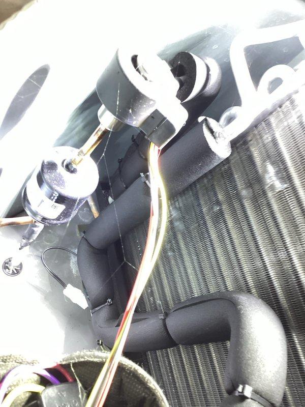 Replaced faulty thermistor on evaporator discharge coil with correct part. The grey-wired thermistor was removed from the evaporator coil assembly near the blower motor, and the new component was properly installed and secured to restore accurate temperature sensing functionality for the HVAC system.