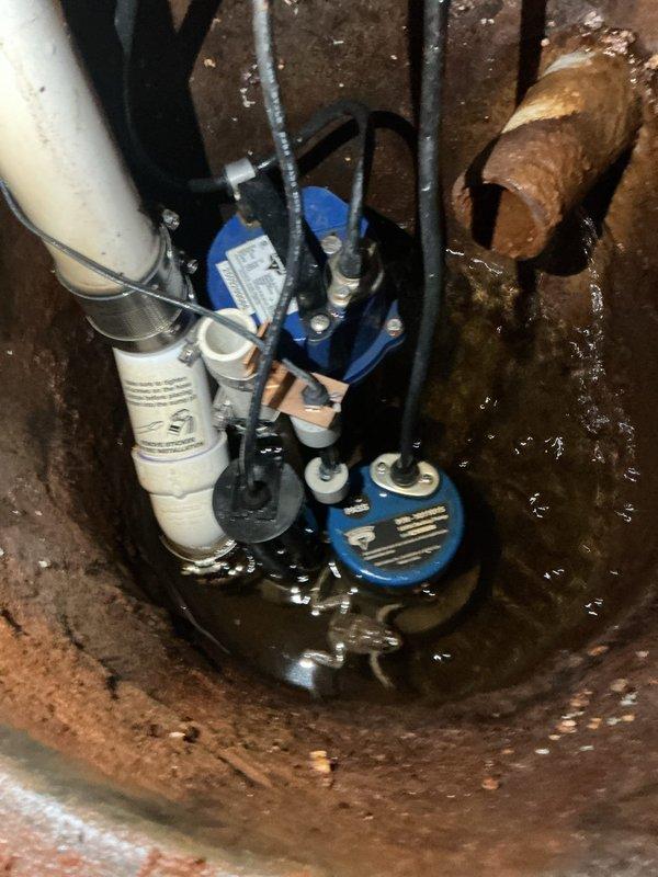 Responded to alarm condition on sump pump system installed under warranty. Upon arrival, inspected primary and backup pump assembly in basement sump pit and determined backup pump had activated due to operational issue. Verified system functionality, checked discharge piping connections, and confirmed proper pump operation. Documented existing conditions including significant corrosion on pit walls and surrounding surfaces, though pump equipment remained in serviceable condition. System restored to normal operation with both primary and backup pumps functioning as designed.