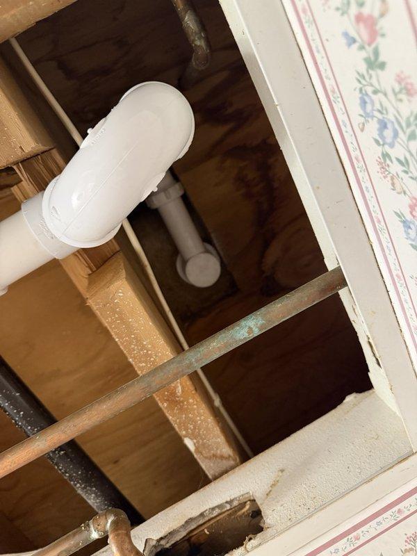 Responded to recurring upstairs bathroom tub leak reported on third service visit. Conducted comprehensive leak testing by filling tub twice with five-minute intervals between draining cycles. Performed thorough visual inspection of tub spout, overflow assembly, and valve cover while actively splashing water on all fixtures to identify potential leak sources. Verified all compression nuts were dry with no moisture present. Accessed ceiling cavity below tub to inspect drain assembly and surrounding plumbing infrastructure. During inspection, discovered loose valve cover on downstairs shower near the suspected leak area. Tightened shower faceplate securely to wall to prevent water intrusion behind shower enclosure. No active leaking observed during testing procedures. Documented findings with photos of exposed plumbing infrastructure and ceiling-mounted fixture.