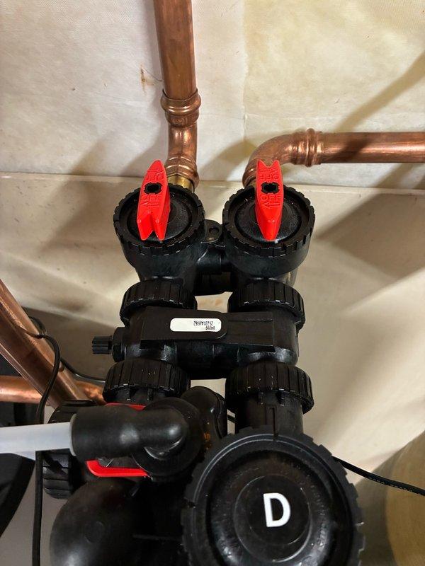 Installed a bypass assembly with integrated bleeder valve on the hydronic heating system manifold. The installation included two red-handled ball valves mounted to black plastic manifold bodies with copper piping connections, along with circulation pump components to allow for proper system maintenance and air purging capabilities.