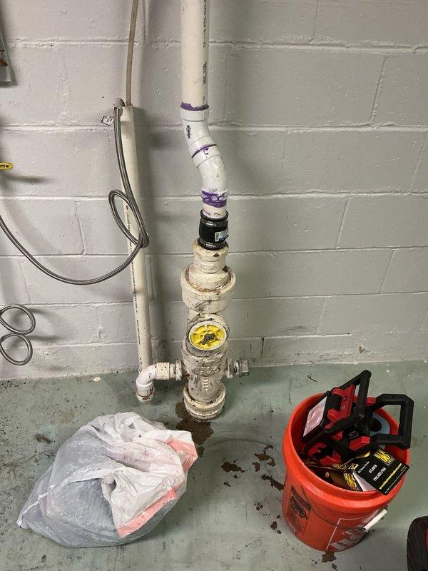 Responded to main line sewer backup occurring during washer use. Performed cable cleaning and video camera inspection of the line. Camera revealed significant structural damage with approximately 1-2 feet of missing pipe section directly below the stack. Encountered a large root intrusion at 50-60 feet that could not be penetrated with standard equipment, along with additional root growth at 93 feet. Documented findings with photographic evidence showing the utility room floor drain area and plumbing stack assembly. Recommended immediate pipe repair for the damaged section and professional root removal service to restore proper drainage function.
