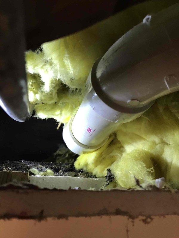 Responded to service call for multiple plumbing issues including inadequate water supply to refrigerator from main line, leak under kitchen sink drain line, and leak at bathroom bathtub. Inspected piping in crawl space/attic area where PVC supply line penetrates through insulation and identified supply line concerns. Accessed ceiling cavity above bathtub to investigate leak source and assess plumbing configuration. Documented conditions with photographs and provided detailed repair estimate to address all identified leaks and water supply deficiencies.