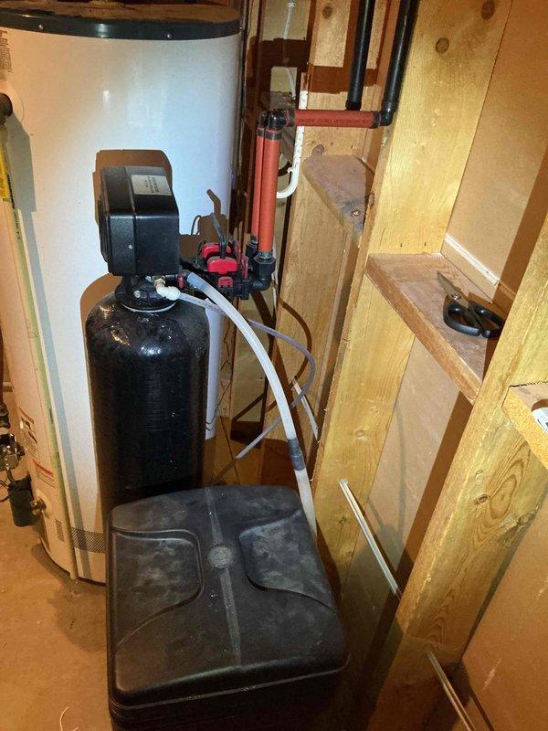 Inspected the existing water softener, which was not drawing salt from the brine tank and was no longer delivering softened water. Evaluated the control valve, resin tank, brine tank, and plumbing connections, and determined the unit is older and undersized for the household demand. Assessed the adjacent power-vent water heater and surrounding piping, and documented existing equipment to prepare estimates for a replacement softener, carbon filtration tower, and water heater.