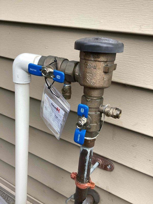 Performed annual backflow test on the irrigation system's Pressure Vacuum Breaker (PVB) assembly, which is wall-mounted at the exterior of the home and equipped with Wilkins shutoff valves and accessible test cocks. The assembly was confirmed testable and was tested in accordance with standard PVB test procedures. Note: the supporting galvanized riser pipe shows surface corrosion and a rusted mounting bracket, which may warrant future attention.
