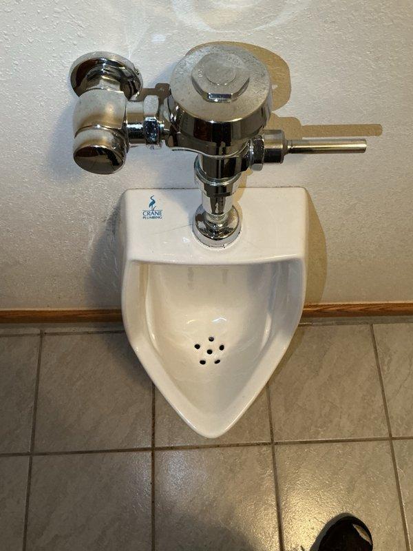 Responded to a wall-mounted urinal that ran continuously and required the water supply to be shut off to stop it. Diagnosed the chrome flush valve as worn and at end of life, causing the constant running. Submitted a parts order for a replacement urinal flush valve.