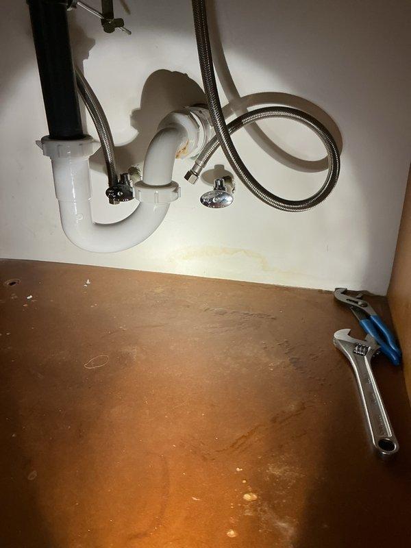 Removed the seized multi-turn angle stop valves beneath the master bathroom vanity and installed new shutoff valves with the braided stainless steel supply lines reconnected. The cabinet interior was inspected, with minor staining and discoloration noted on the back wall and cabinet floor, and the P-trap and drain connections were checked and left in place.