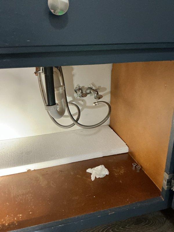 Removed the seized multi-turn angle stop valves beneath the master bathroom vanity and installed new shutoff valves with the braided stainless steel supply lines reconnected. The cabinet interior was inspected, with minor staining and discoloration noted on the back wall and cabinet floor, and the P-trap and drain connections were checked and left in place.