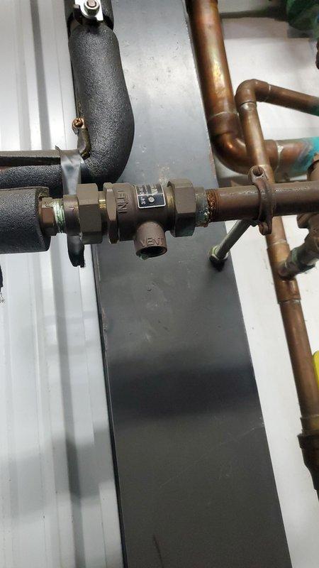 Responded to an active water leak at the backflow preventer assembly, which was discharging heavily enough to fill a 5-gallon bucket and had saturated the surrounding concrete floor. Inspected the backflow device and adjacent brass relief valve and piping, noting corrosion and mineral residue at the threaded connections. Submitted a parts order for a backflow preventer rebuild kit to restore proper sealing and complete the repair.