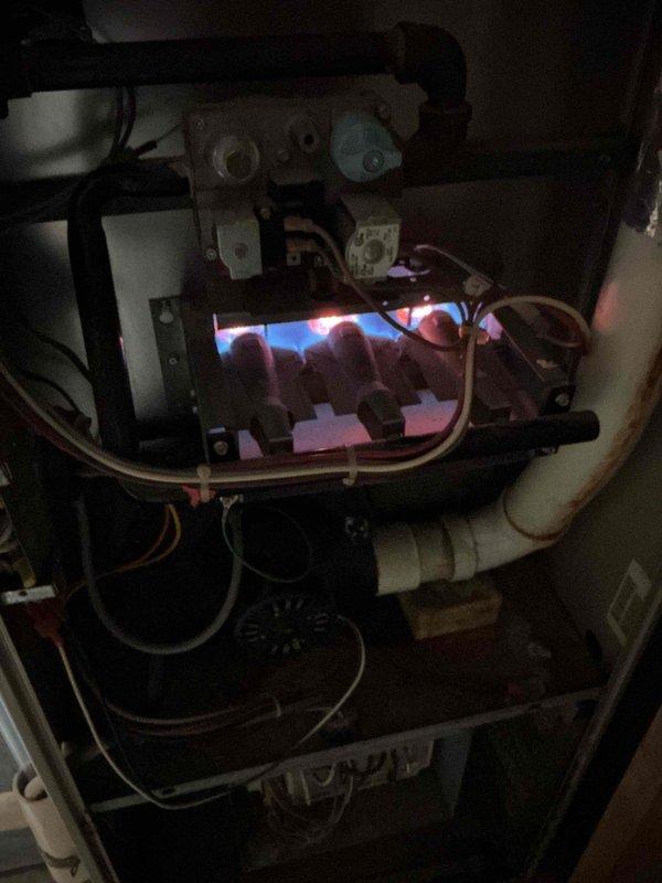 Diagnosed a no-heat condition on a 25+ year old gas furnace: the inducer motor was running but the hot surface igniter never energized, indicating a pressure switch circuit problem. Shut down the unit and cleared a restriction in the pressure switch tubing by blowing compressed air through the line to the inducer housing. Restored power, and the furnace completed its full ignition sequence with stable burner flame and is now heating properly.
