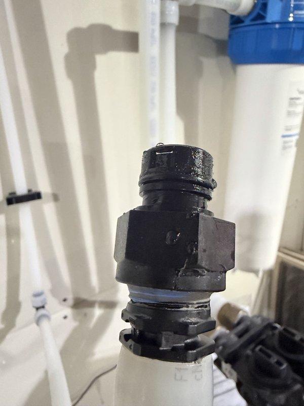 Responded to a warranty call for a water softener leaking at the control head and drain fitting. Inspected the Fleck valve assembly and found the drain line fitting weeping at the threaded connection, with water pooling on the floor beneath the resin tank. Replaced the defective drain fitting, resealed the connection, and verified a leak-free operation under pressure.