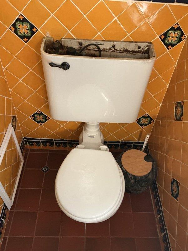 Responded to a water leak from the upstairs bathroom dripping into the downstairs kitchen and traced the source to the base of an aging toilet. Inspected the toilet and tank, which showed heavy mineral buildup, staining, and corrosion on the supply valve and internal components. Documented conditions and provided an estimate for the customer's requested ADA-height toilet replacement and supply line repipe.