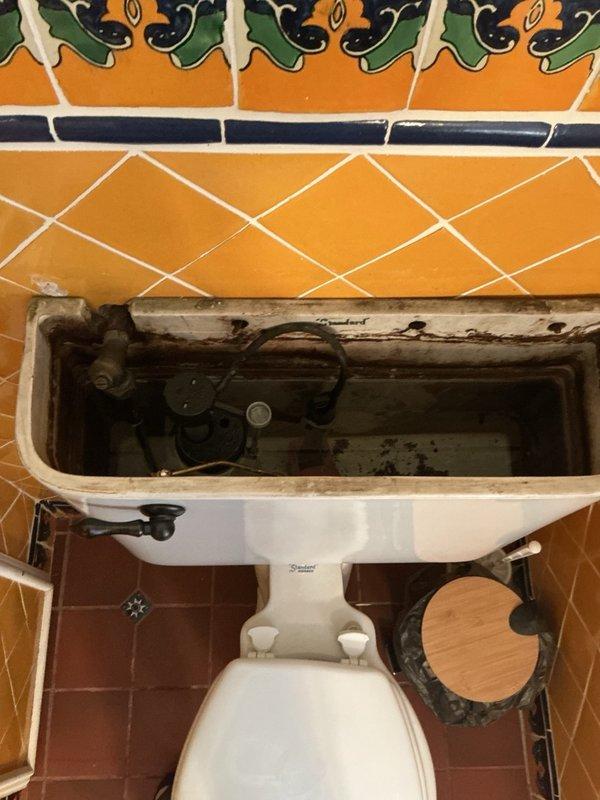 Responded to a water leak from the upstairs bathroom dripping into the downstairs kitchen and traced the source to the base of an aging toilet. Inspected the toilet and tank, which showed heavy mineral buildup, staining, and corrosion on the supply valve and internal components. Documented conditions and provided an estimate for the customer's requested ADA-height toilet replacement and supply line repipe.