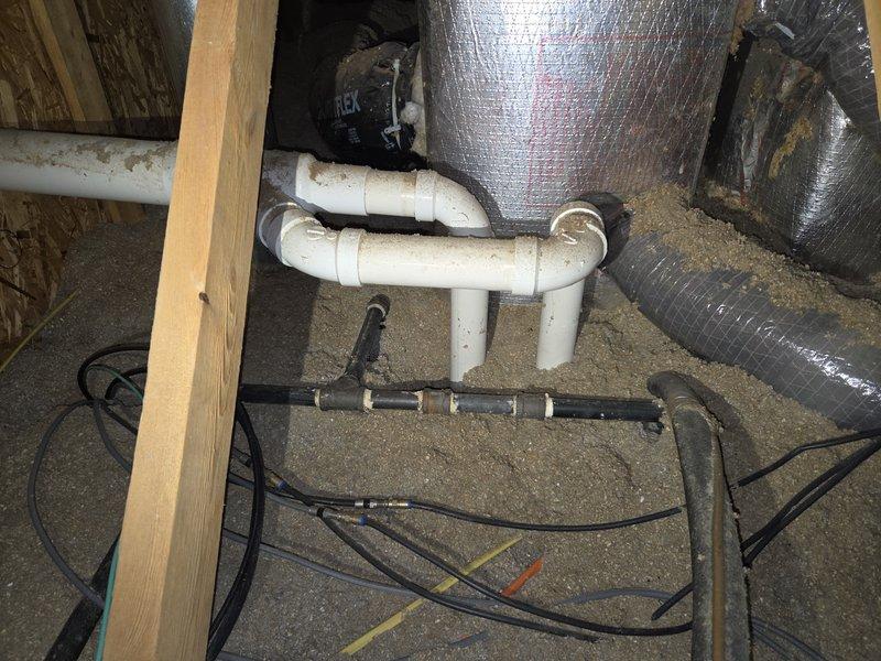 Responded to service call for water leaking from ceiling originating in attic area. Upon inspection, discovered condensation accumulation on HVAC ductwork and associated plumbing systems in attic space. Examined white PVC condensate drain lines and U-trap configuration, noting dust and dirt buildup on piping surfaces. Inspected black metal manifold distribution system and surrounding electrical routing. Assessed reflective silver ductwork insulation showing moisture droplets and condensation on metallic surface, indicating potential insulation degradation or inadequate vapor barrier. Evaluated horizontal black pipe with visible mineral deposits and white residue suggesting ongoing moisture issues. Photographed affected areas including PVC plumbing configuration, gray elbow fittings, and condensate management system. Documented conditions of confined attic utility space where HVAC, plumbing, and electrical systems converge. Identified condensation on ductwork insulation as primary sourc