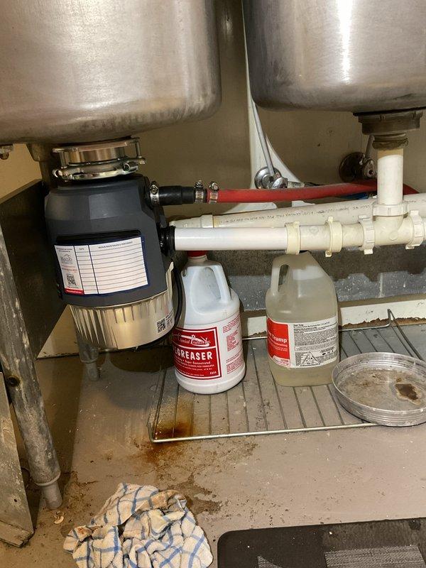 Installed a new 1-horsepower garbage disposal unit under a double-basin stainless steel kitchen sink. The installation included proper connection of white PVC drain piping and integration with existing plumbing infrastructure, including a shut-off valve for water supply control.