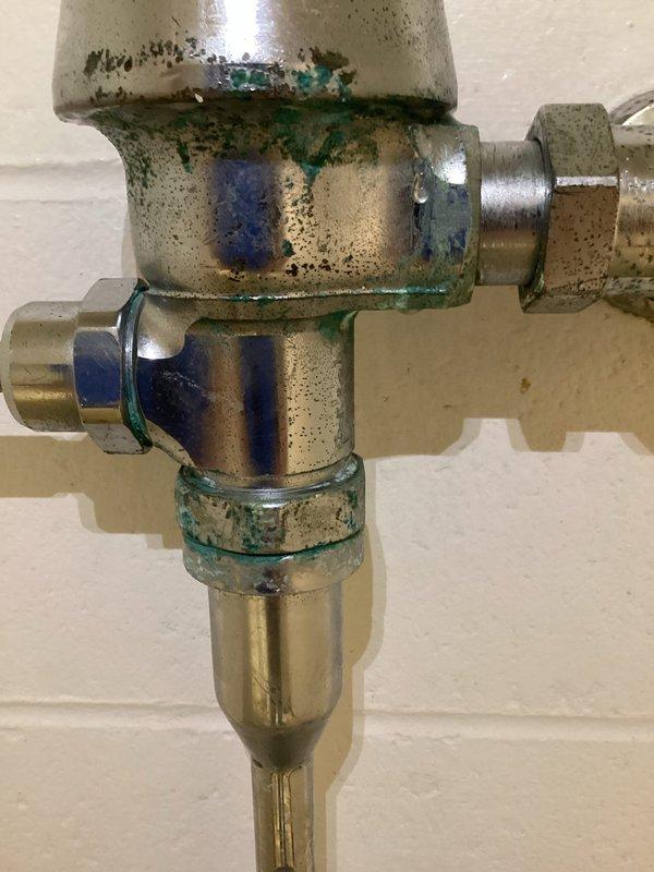 Responded to water leak at basement bathroom urinal with inoperable shut-off valve. Upon inspection, found heavily corroded brass supply valve assembly with significant verdigris buildup and mineral deposits affecting operation. Replaced defective shut-off valve, restored proper water control to wall-mounted urinal fixture, tested flush mechanism for proper operation, and verified all connections were leak-free.
