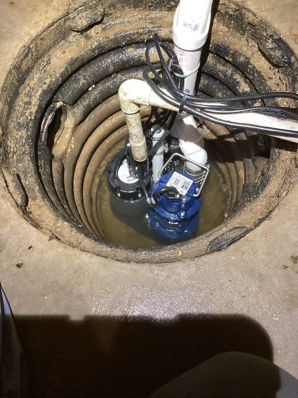 Installed PHCC battery backup combination sump pump system in basement sump basin. The installation included mounting the primary blue pump unit in the circular concrete basin, connecting multiple discharge pipes including white PVC piping, and routing electrical cables for power supply. Configured the battery backup system to provide emergency pumping capability during power outages, ensuring continuous flood protection for the property.
