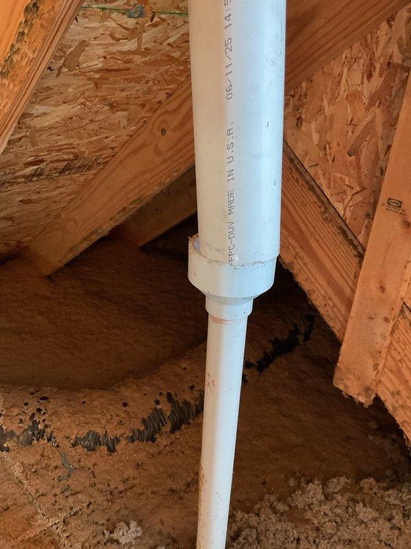 Responded to coordinate plumbing work with roofing contractor for sewer vent installation through roof penetration. Inspected white PVC vent pipe running vertically through attic space and wooden framing members to ensure proper alignment and structural clearance. Applied solvent cement to PVC joints and connections, including copper-colored elbow fitting, to create watertight seals per code requirements. Verified pipe positioning, slope, and secure mounting before roofers installed flashing boot and completed roof penetration. Confirmed all plumbing connections were properly glued and system was ready for final roofing work.