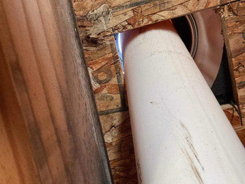 Responded to coordinate plumbing work with roofing contractor for sewer vent installation through roof penetration. Inspected white PVC vent pipe running vertically through attic space and wooden framing members to ensure proper alignment and structural clearance. Applied solvent cement to PVC joints and connections, including copper-colored elbow fitting, to create watertight seals per code requirements. Verified pipe positioning, slope, and secure mounting before roofers installed flashing boot and completed roof penetration. Confirmed all plumbing connections were properly glued and system was ready for final roofing work.