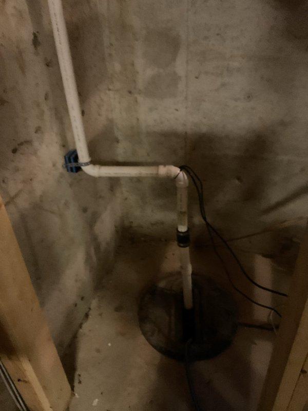 Performed inspection and evaluation of existing sump pump system per customer request to assess current discharge configuration and explore alternative routing options. System was found to be operational but functioning below optimal efficiency. Examined white PVC discharge piping with dual ball valves, vertical run through floor joists, and connection points in basement area. Assessed pump unit positioning on concrete floor, electrical connections, and current discharge path routing along foundation walls. Identified opportunities for system modification to improve discharge flow and overall performance. Documented existing installation with photographs showing piping layout, valve configuration, and pump placement for reference in developing recommended modifications to enhance system effectiveness.