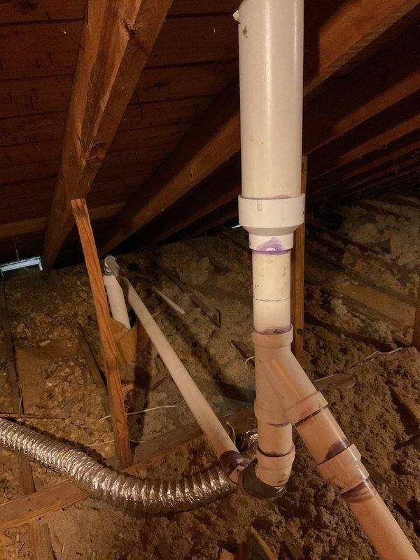 Responded to repair damaged plumbing exhaust vent lines in attic space that were broken during recent roof installation. Accessed attic area and inspected white PVC vent piping with purple primer markings running vertically through roof structure. Assessed damage to vent stack and connections where roofing contractor had compromised the existing plumbing ventilation system. Repaired and reinstalled proper venting configuration to restore functionality of plumbing exhaust lines, ensuring all connections were secure and properly sealed. Verified vent pipes extended correctly through roof penetrations and all joints were watertight to prevent future leaks or system failures.