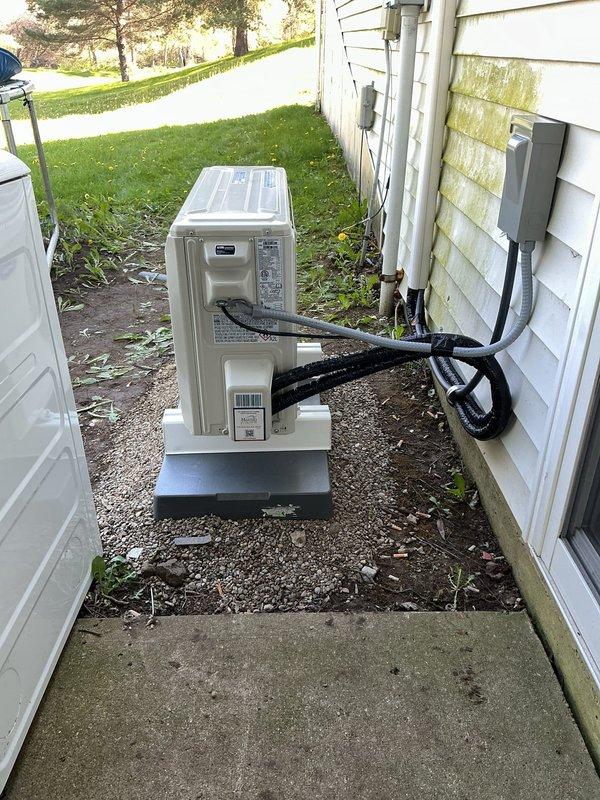 Completed installation of Carrier Performance Series inverter-driven heat pump mini-split system, including model 37MARAQ12AA3 outdoor condenser unit and D5MAHAQ12XA3 variable speed indoor air handler. Mounted indoor evaporator unit on interior wall, positioned outdoor condenser on new 2" PVC pad on gravel base against exterior wall, and ran new 10-foot line set between units with line hide section for aesthetic concealment. Licensed electrician installed high voltage power supply to outdoor unit with new disconnect box and whip. Installed black insulated refrigerant lines secured to exterior siding with clips, connected all refrigerant piping, evacuated system, and charged to manufacturer specifications. Ran white PVC condensate drain line along exterior wall for proper drainage. Performed system startup, verified proper operation of all components including inverter technology and heat pump functionality, and confirmed adequate airflow and temperature differential. Registered manufac