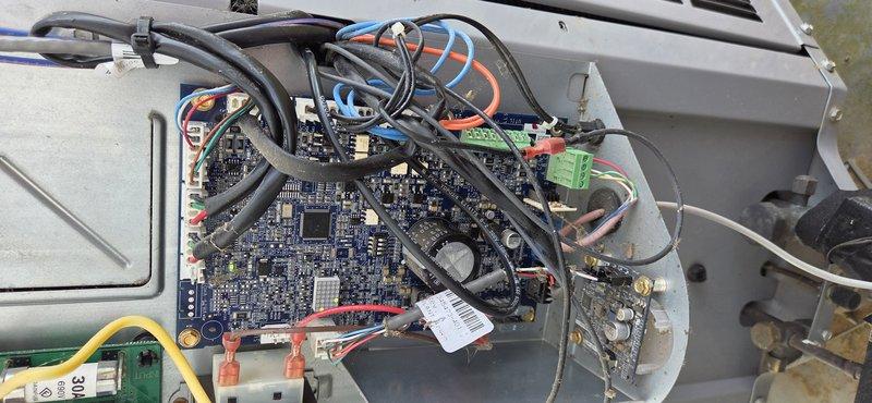 Responded to service call for heat pump outdoor temperature sensor (OST) thermistor issue. Accessed control board assembly and inspected electronic components, wiring connections, and terminal blocks. Documented internal configuration of circuit board including sensor connections and wiring harness. Verified proper connections at green terminal blocks and examined circuit board for any visible damage or loose connections. Photographed control board assembly and sensor wiring for service records.