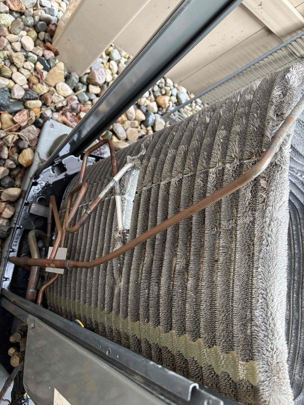 Completed comprehensive air conditioning tune-up and cleaning service on outdoor condensing unit. Coil surfaces showed heavy accumulation of dust, dirt, and debris with visible organic growth and oxidation on aluminum fins. Thoroughly cleaned heat exchanger coils, removed environmental buildup from cooling fins, and inspected copper refrigerant lines and mounting brackets. Unit restored to optimal operating condition for efficient seasonal performance.