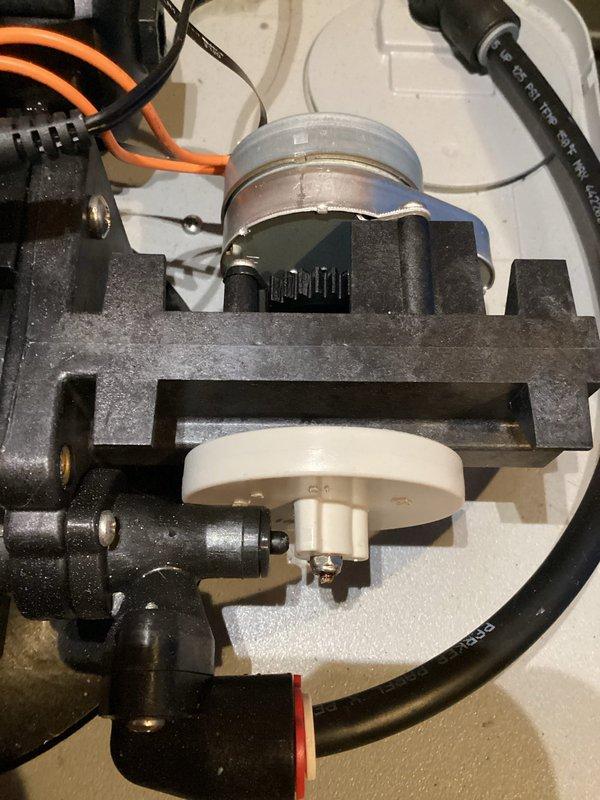 Responded to service call for malfunctioning water softener with water accumulation in the brine tank. Upon inspection of the A.O. Smith water softener system, assessed the control head assembly, pump mechanism, and brine tank condition. Documented the excessive water level in the salt storage area and examined the internal components including the impeller assembly and motor coupling. Evaluated the control valve operation, plumbing connections, and electrical components to determine the cause of improper regeneration cycle. Photographed the pump assembly showing the white impeller disc within the dark metal housing and the overall system installation with visible water contamination in the brine tank.