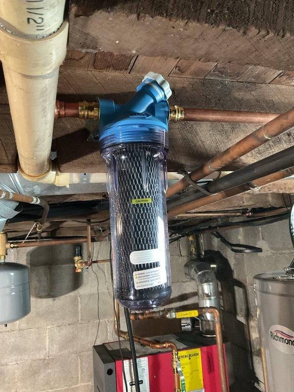 Completed replacement of two water filtration cartridges on existing whole-house water treatment system installed in basement utility area. Removed old filter elements from clear housings mounted on copper supply lines beneath floor joists. Installed new carbon block filter cartridges, ensuring proper seating and O-ring placement. Verified all brass fittings and connections were secure at filter head assemblies with blue caps. Pressurized system and checked for leaks at housing seals and pipe connections. Confirmed proper water flow through filters and verified system operation with no signs of bypass or leakage.