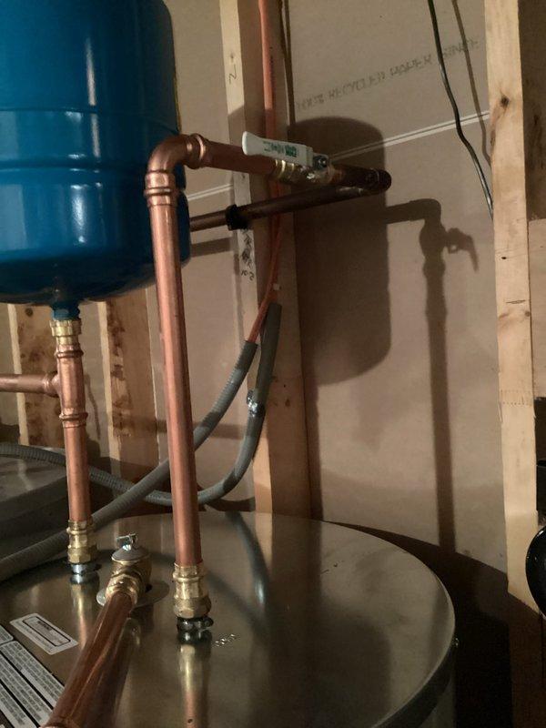 Completed electric tanked water heater installation in residential utility area with two-person crew over three-hour period. Installed new stainless steel water heater tank with copper supply piping, brass compression fittings, and shutoff valves. Connected all necessary plumbing lines including hot and cold water supply connections with proper elbow joints and horizontal runs. Integrated system with existing blue pressure expansion tank and ensured proper electrical connections. All copper piping secured to wall framing with appropriate supports, and installation meets code requirements for residential water heating systems.